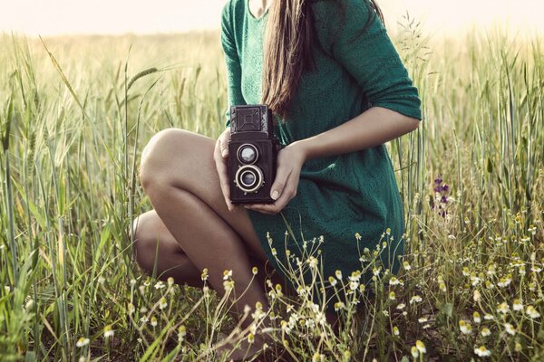 A girl in the grass holds a camera