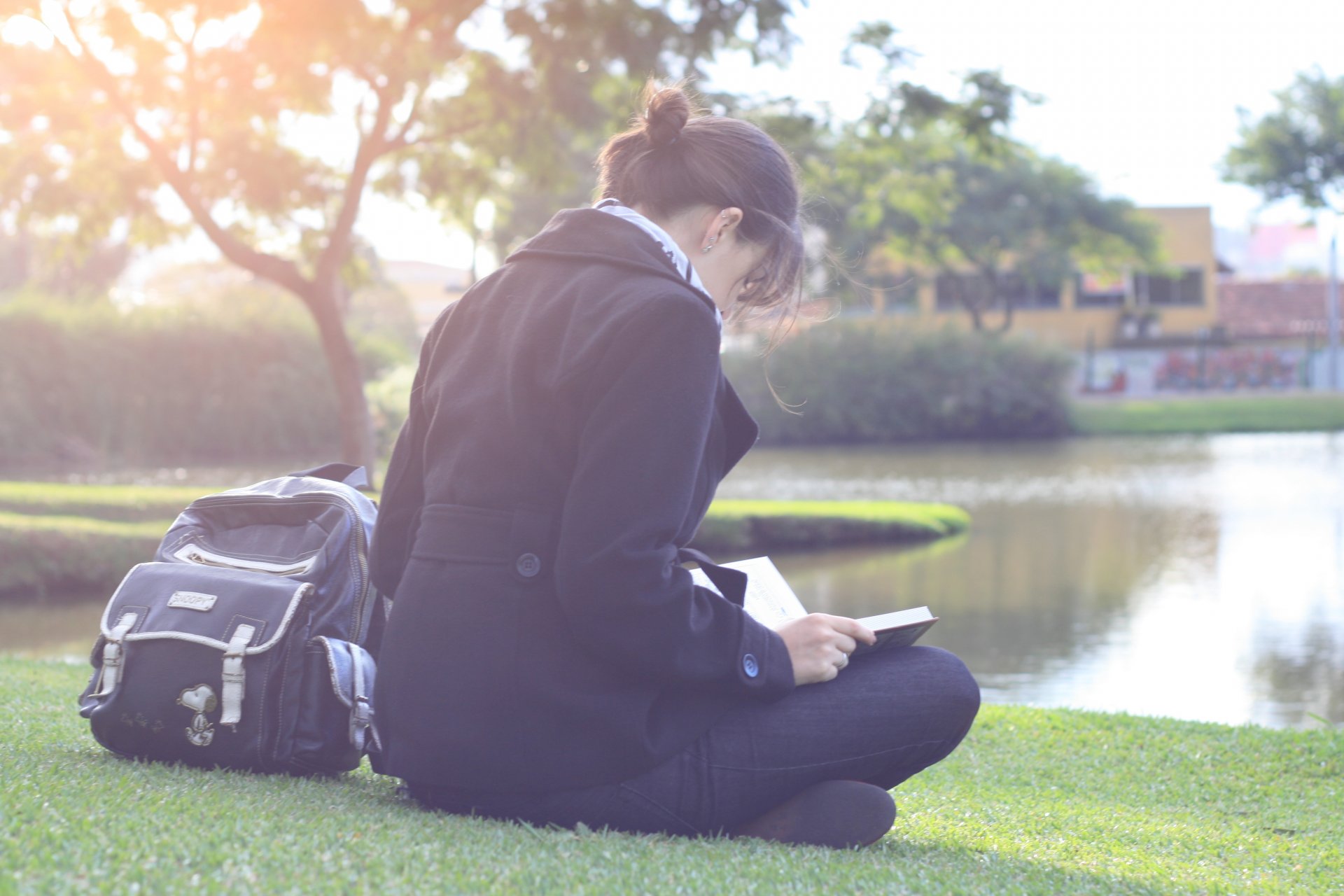 nature landscape girl brunette sitting earth grass greenery tree trees foliage leaves spring autumn reading book. textbook interesting coat jeans scarf river water reflection sun rays ray house houses apartments widescreen wallpaper fullscreen wallpaper