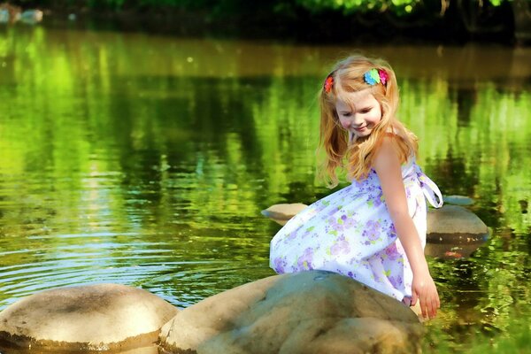 En el caluroso verano, es agradable sentarse en una piedra junto al lago, incluso si eres una niña pequeña