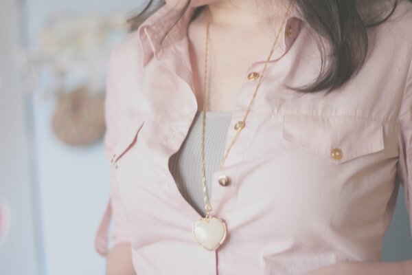 A girl in a light pink blouse. Heart-shaped pendant