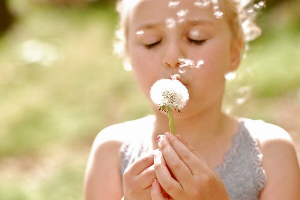 A girl blowing out a dandelion in a gray lace dress