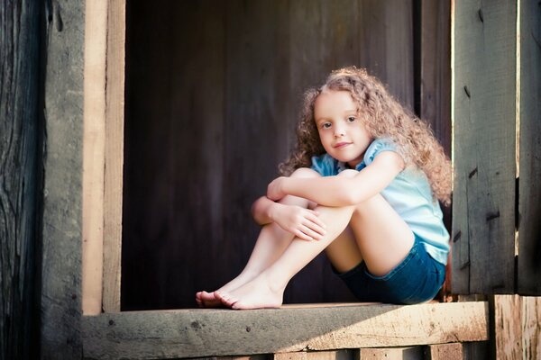 A girl with curly hair is sitting on the porch