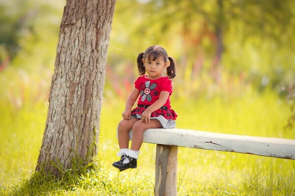 Petite fille sur un banc dans une forêt ensoleillée