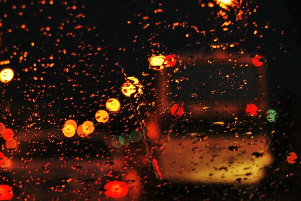 Las luces de la ciudad de la noche a través de las gotas en el cristal