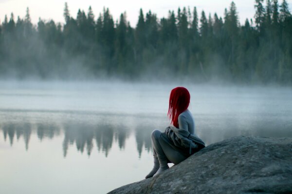 Fille aux cheveux rouges est assis sur le rivage et regarde dans le brouillard