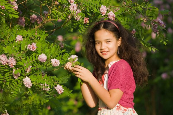 Una niña sostiene una rama de arbusto con flores Rosadas