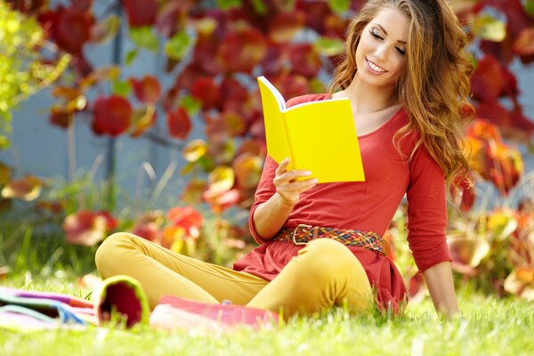 A young girl reads in autumn on the grass