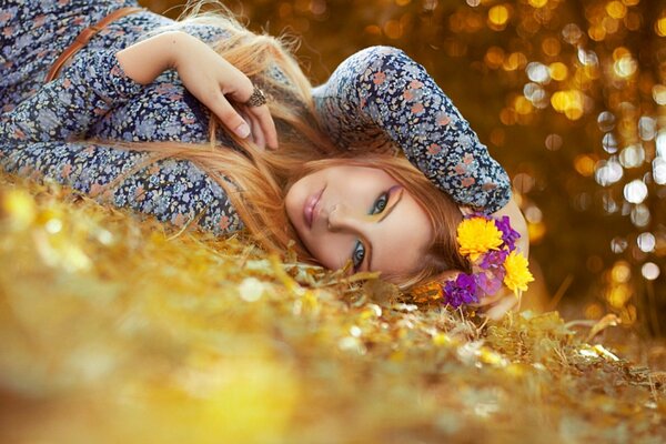 A girl in a colorful dress and with flowers in her hair lies among autumn leaves