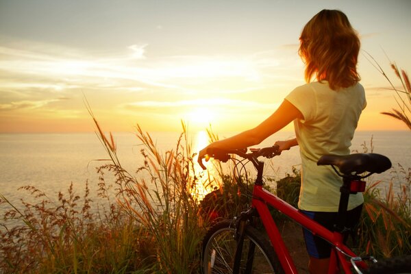 A girl with a bicycle looks at the sunset