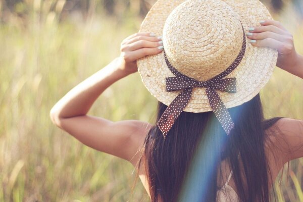 Ragazza bruna in posa in un cappello sul campo nel verde