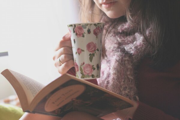 Fille en pull lit un livre et boit du thé