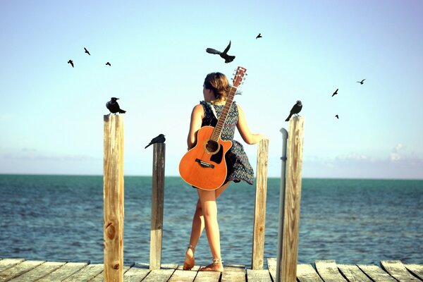 Fille avec une guitare debout sur le bord de la mer