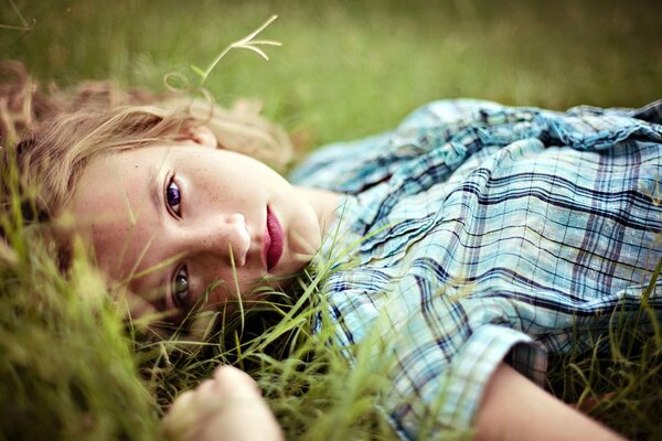 Fille blonde en portrait se trouve sur l herbe, regardant pensivement dans la caméra