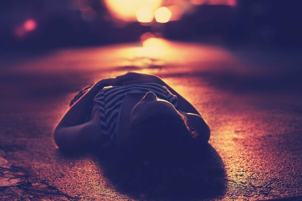 A girl lying on the asphalt under the evening lights