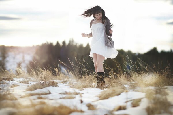 Una chica con un vestido y botas en el campo con la nieve derretida de la primavera