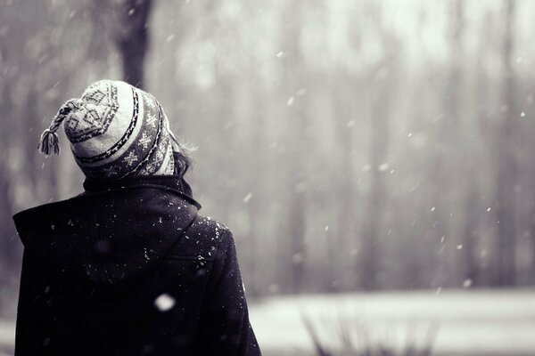 Fille dans un chapeau en regardant la neige qui tombe