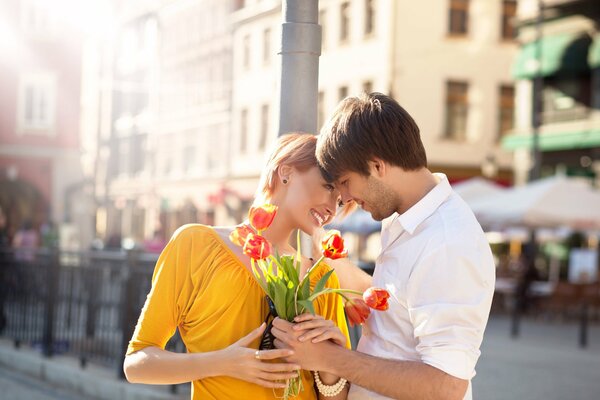 Ein Mädchen und ein Mann bei einem romantischen Date an einem sonnigen Tag in der Stadt mit einem Strauß roter Tulpen