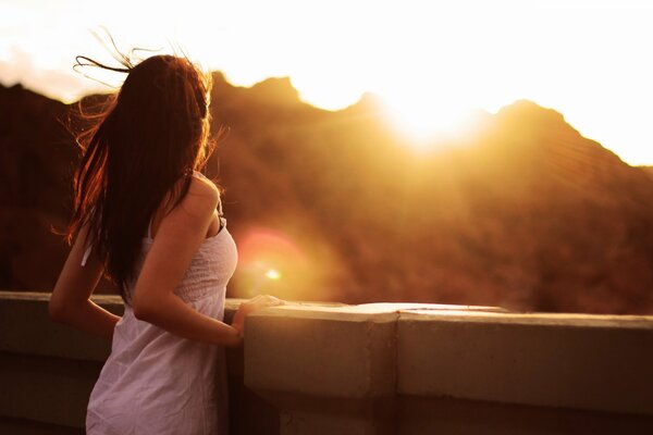 A girl in a white dress looks at the sunset