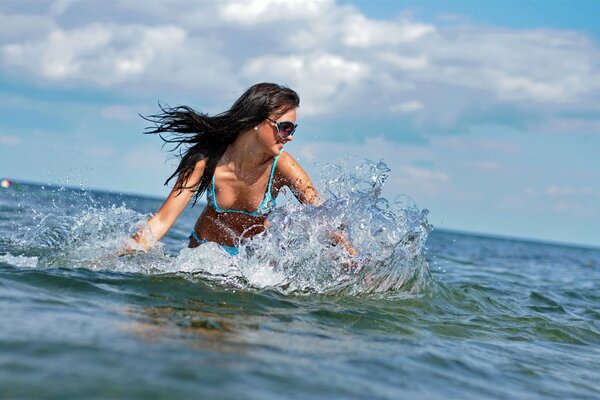 Slender girl with dark hair wearing glasses, swimming in the sea. She smiles, enjoys the good sunny weather