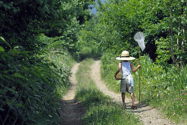 Garçon dans un chapeau avec une épuisette marchant le long du chemin