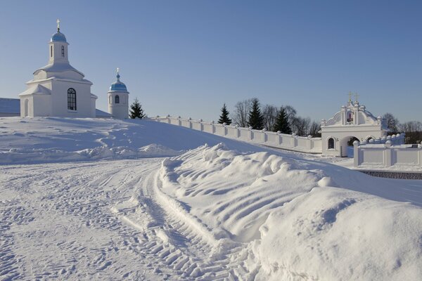 The white monastery stands on a steep snow-covered hill against a clear blue sky