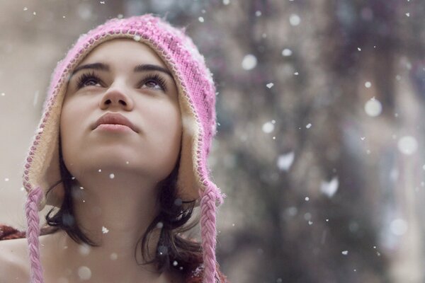 Chica con sombrero de invierno mirando copos de nieve