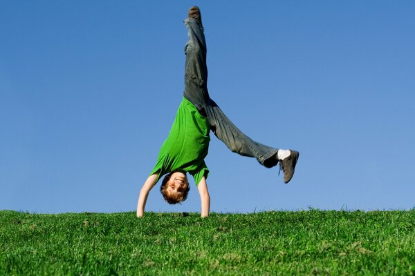 The boy is standing upside down on the grass