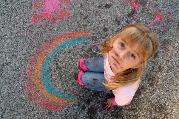 Niña manchada dibuja un arco iris en el asfalto