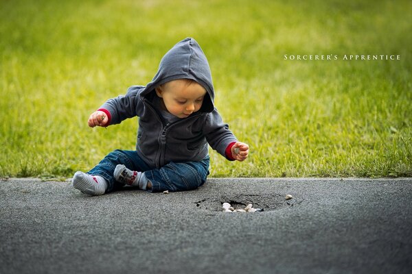 Ein Junge auf der Straße sitzt auf dem Asphalt auf dem Hintergrund des Grases