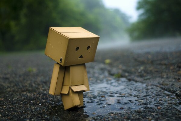 A box in the shape of a robot is sad on the asphalt