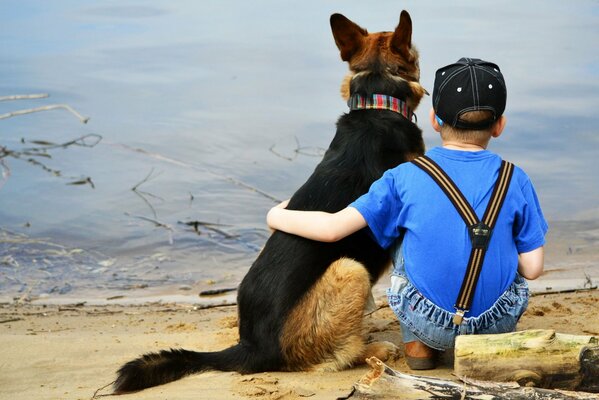 Un niño abraza a un perro en la orilla del lago