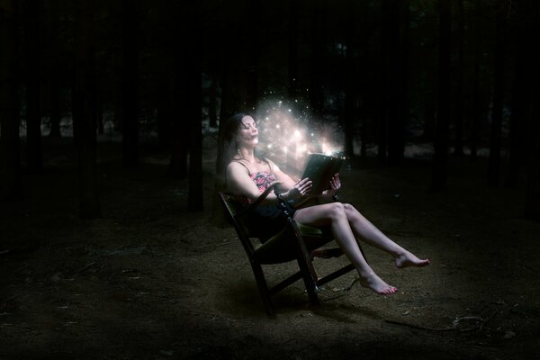 A brown-haired girl is sitting in the night forest with a magic book