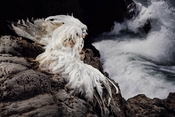 A girl in a bird costume is sitting on the rocks