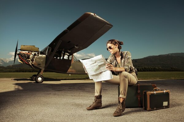 Das Mädchen mit der Karte in der Hand sitzt auf Koffern neben dem Flugzeug