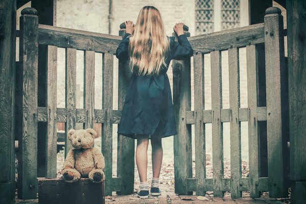 A girl with a suitcase looks through the gate