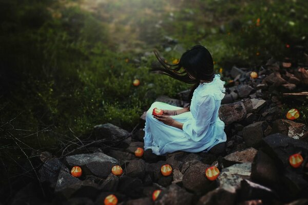 A girl in a white dress sitting on the rocks with an apple in her hand