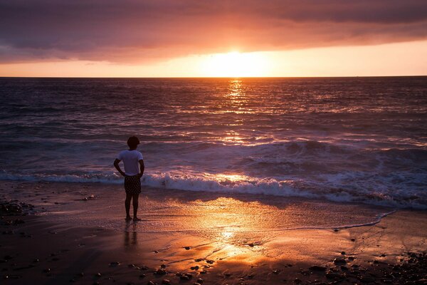 Hombre viendo la puesta de sol en la orilla del mar