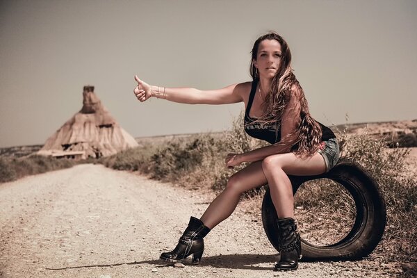 A girl sits on a tire next to the road and votes