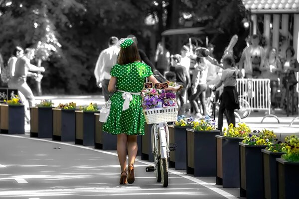 A girl in a green dress is driving a bicycle with flowers