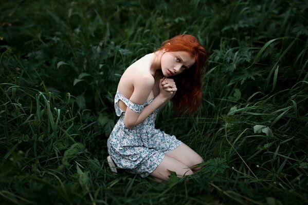 A red-haired defenseless girl with a bare shoulder on the grass