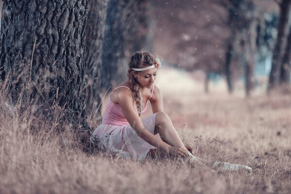 Une fille de ballerine assise près d un arbre, le met sur les pointes