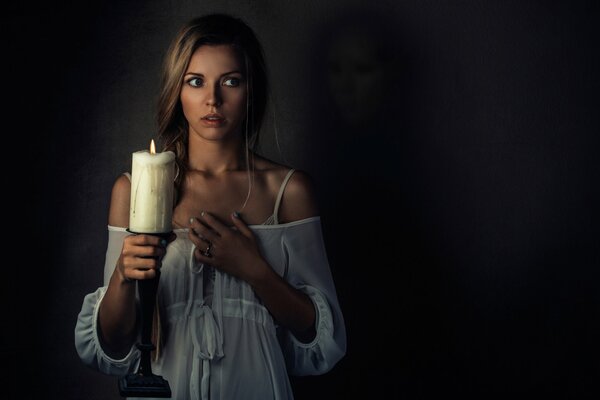 A girl with a candle in her hand saw a ghost and is afraid