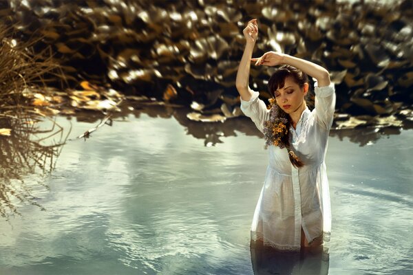 A girl with flowers in braids and in a nightgown is standing in the water