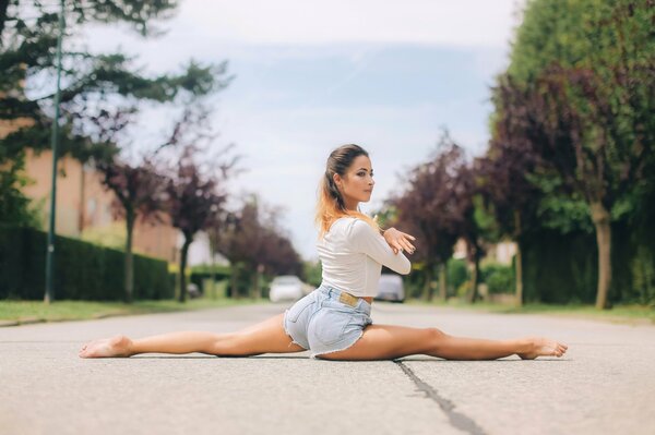 Su strada ragazza in pantaloncini facendo stretching spago