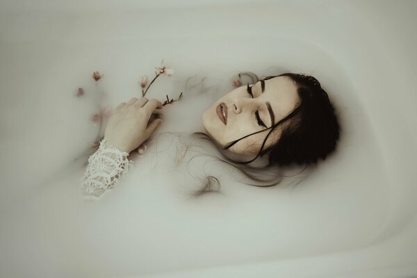 The girl is lying in the bathtub surrounded by flowers