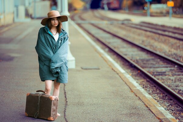 Hermosa chica en la estación de tren con una maleta