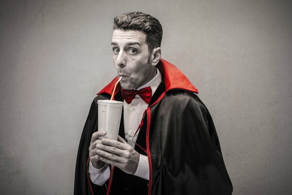 A man in a Dracula costume drinks juice from a straw