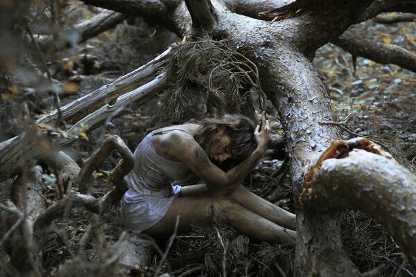 Hermosa chica sentada en el bosque sucio, alrededor de los árboles