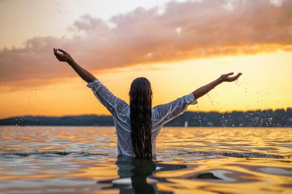 The girl is standing waist-deep in the water against the sunset