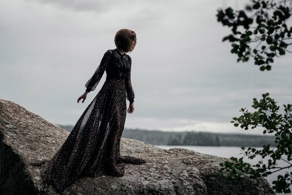 Mädchen in einem schönen Kleid auf einem Stein in der Nähe des Meeres